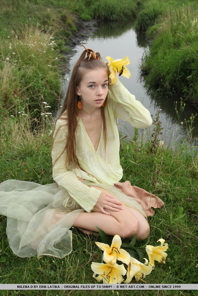 Молоденькая красотка голой позирует на поляне возле озера и лилиями ласкает волосатую киску и красивую грудь