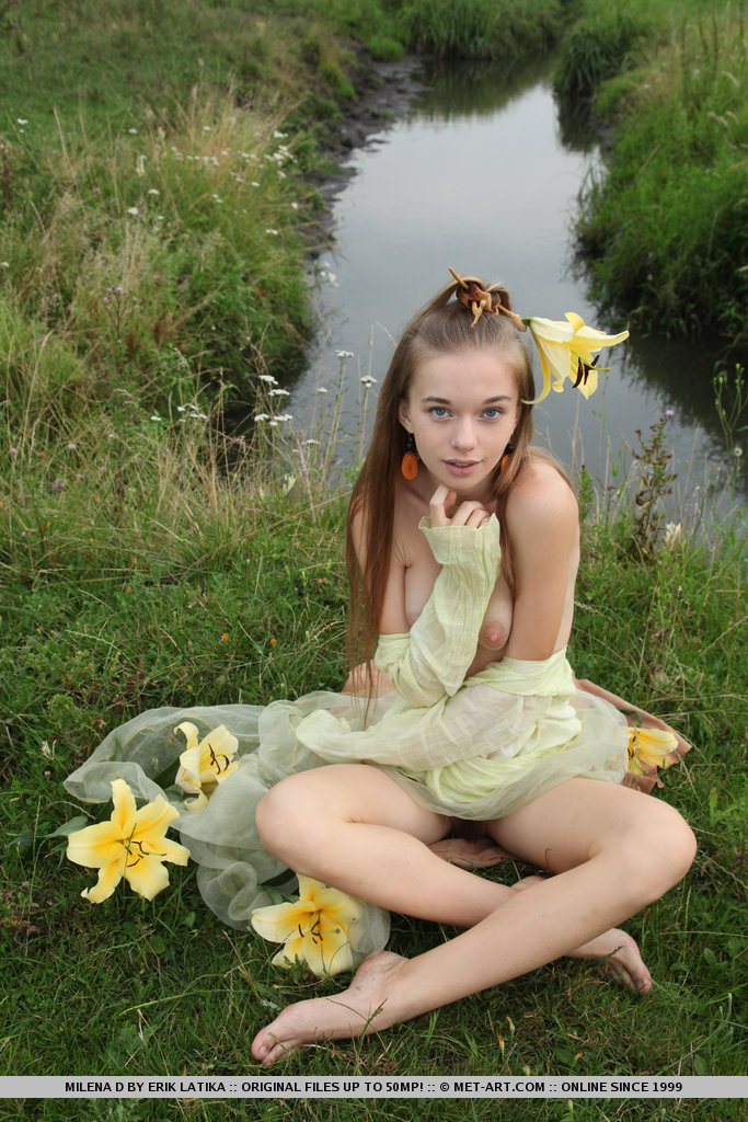 Молоденькая красотка голой позирует на поляне возле озера и лилиями ласкает волосатую киску и красивую грудь